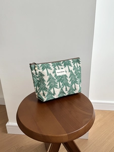 Detailed view of canvas makeup bag with green pine trees and bronze zipper pull