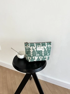Detail of embroidered pine tree pattern on beige canvas makeup bag with brown zipper