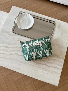 Detail of linen makeup bag featuring green pine tree prints and woven brand label