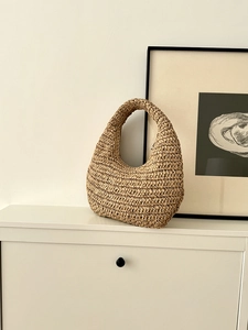 Detailed close-up of a handmade woven hobo bag with beige raffia texture on white shelf