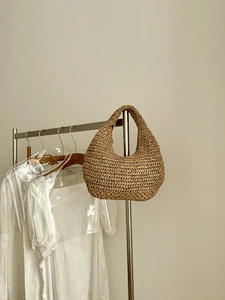 Detail of hand-woven hobo shoulder bag with textured straw pattern on a metal hanger