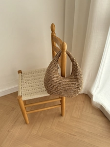 Detail of hand-woven straw shoulder bag on wooden chair with natural hobo texture