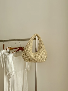 Detail of hand-woven straw hobo shoulder bag hanging on a minimalist silver hanger