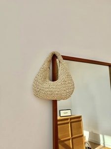 Macro detail of hand-woven beige straw cloud bag texture on a dark wooden frame