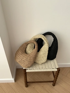 Three hand-woven cloud hobo bags in brown, beige and black displayed on a wooden stool