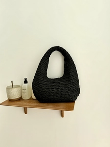 Handwoven black cloud shoulder bag with minimalist semi-moon design on a wooden shelf