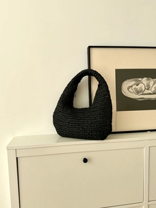 Detail of black woven straw handbag showing the texture and half-moon handle design