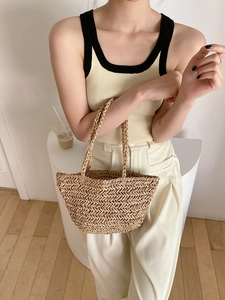 Close-up detail of the woven V-pattern texture and handle on a straw beach handbag