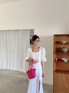 Close-up of bright pink hand-woven straw tote bag paired with a white linen dress outfit