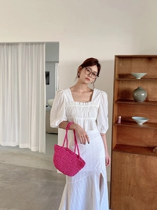 Detail of a white puff sleeve top and high waist slit skirt with a pink woven handbag