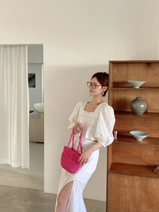 Close-up of a pink hand-woven straw handbag paired with a white puff sleeve summer outfit