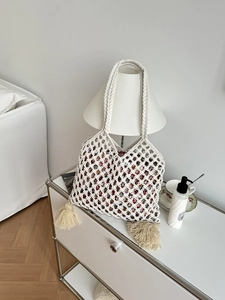 Détail macro du sac cabas tissé beige avec doublure fleurie et pompons sur le côté