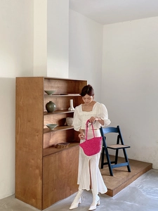 Close-up of bright fuchsia straw woven handbag held by model in elegant summer outfit