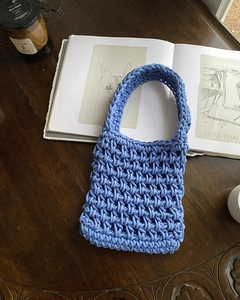 Flat lay of light blue hand-woven handbag with honeycomb texture on dark wooden table
