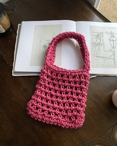 Detail shot of handwoven fuchsia knit handbag on a rustic wooden table with a candle