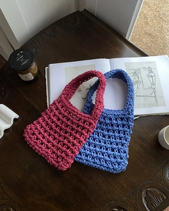 Detail of handmade knit handbags in rose red and blue mesh weave on a wooden table