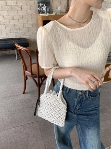 Détail d'un sac à main tissé blanc crème assorti à un chemisier à manches bouffantes