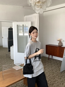 Détail d'un sac seau en maille noire tenu par un mannequin en T-shirt gris imprimé