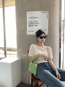 Photo lifestyle d'un sac à main tissé vert porté avec un haut blanc à manches bouffantes