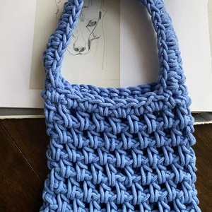 Light blue handmade crochet mini handbag with hollow woven texture on dark wooden background