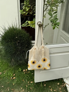 Detail of crochet sunflower tote bag with tassel drawstring hanging on garden gate