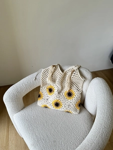 Close-up of hand-woven sunflower crochet bag with decorative fringe on a soft texture