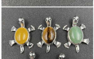 Detail of tortoise pendants with tiger eye, jade, and yellow agate stones on grey surface