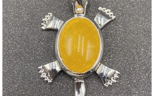 Detailed view of turtle pendant with large oval yellow stone and silver metal finish