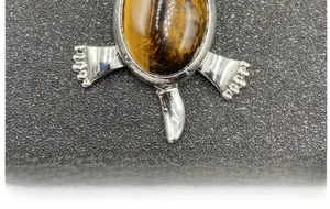 Detailed macro view of turtle pendant featuring a natural oval tiger eye stone inlay