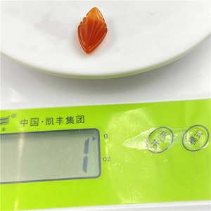 Detailed view of carved orange magnolia petal pendant on a digital scale weighing 1g