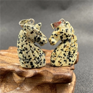 Macro shot of two carved spotted stone horse head pendants on a carved wood base