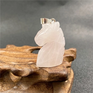 Macro view of pink crystal unicorn pendant with silver bail on a rustic wooden base