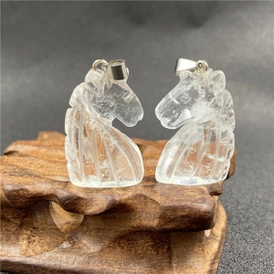 Detailed view of two carved clear quartz unicorn horse head pendants on a wooden base