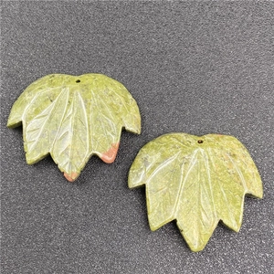 Detailed view of two maple leaf shaped green stone pendants with natural vein patterns