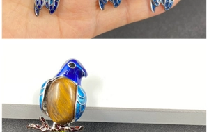 Macro shot of bird brooch with blue enamel wings and brown tiger eye stone setting