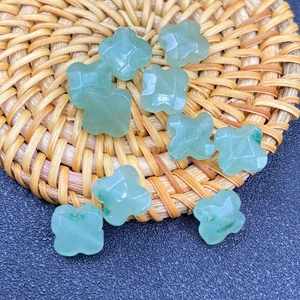 Detail of ten faceted light green aventurine clover beads on a textured surface