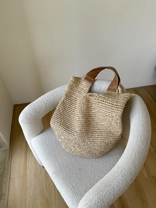 Close-up of woven straw tote bag with brown leather handles on a white textured chair