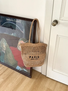 Detail der gewebten Strohtasche mit Paris-Stickerei an einer weißen Holztür hängend