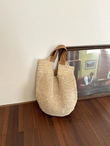 Close-up of the woven straw texture and premium brown leather handle on a beige tote