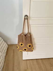 Detail of sunflower crochet tote bag in dark khaki cotton hanging on a white wooden door