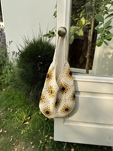 Close-up of handmade sunflower crochet tote bag with ivory yarn on a white wooden door