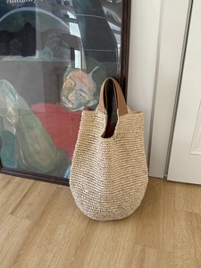 Close-up of the woven texture and brown leather handles on a white straw beach tote bag