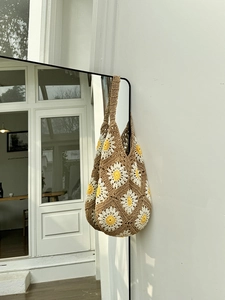 Detail of handmade crochet tote bag featuring white daisy flowers and brown woven texture