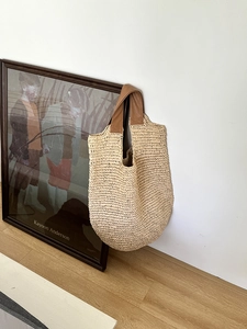 Detail of hand-woven straw shoulder bag with brown leather handle on a white wall