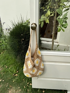 Close-up of handmade crochet hobo bag with white and yellow daisy patterns on garden door