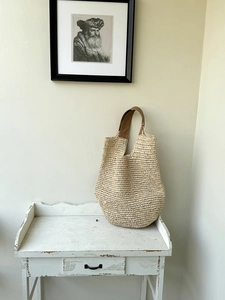 Detailed view of woven straw half-moon bag featuring brown leather handles and textured knit