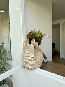 Detail of the woven hollow pattern and brown leather handle on a large straw tote bag