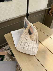 Detail of hollow diamond-patterned crochet tote bag in beige on a wooden cafe table