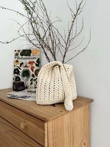 Detail of cream crochet shoulder bag with hollow knit patterns on a wooden cabinet