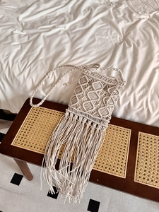 Detail of bohemian cream macrame shoulder bag with long handmade fringe on vintage wood stool